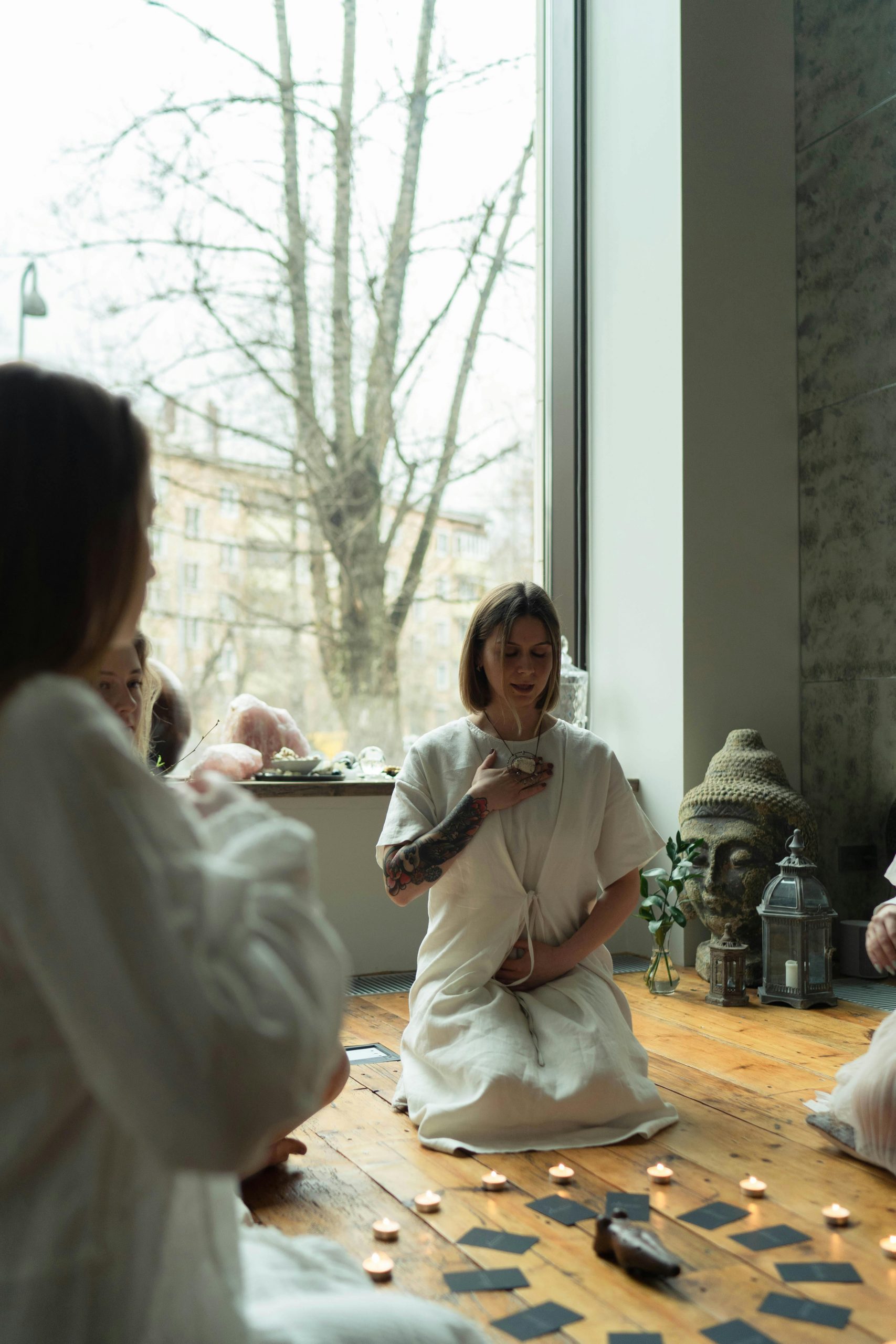 Women engage in a spiritual ritual with candles and cards in a serene indoor setting.